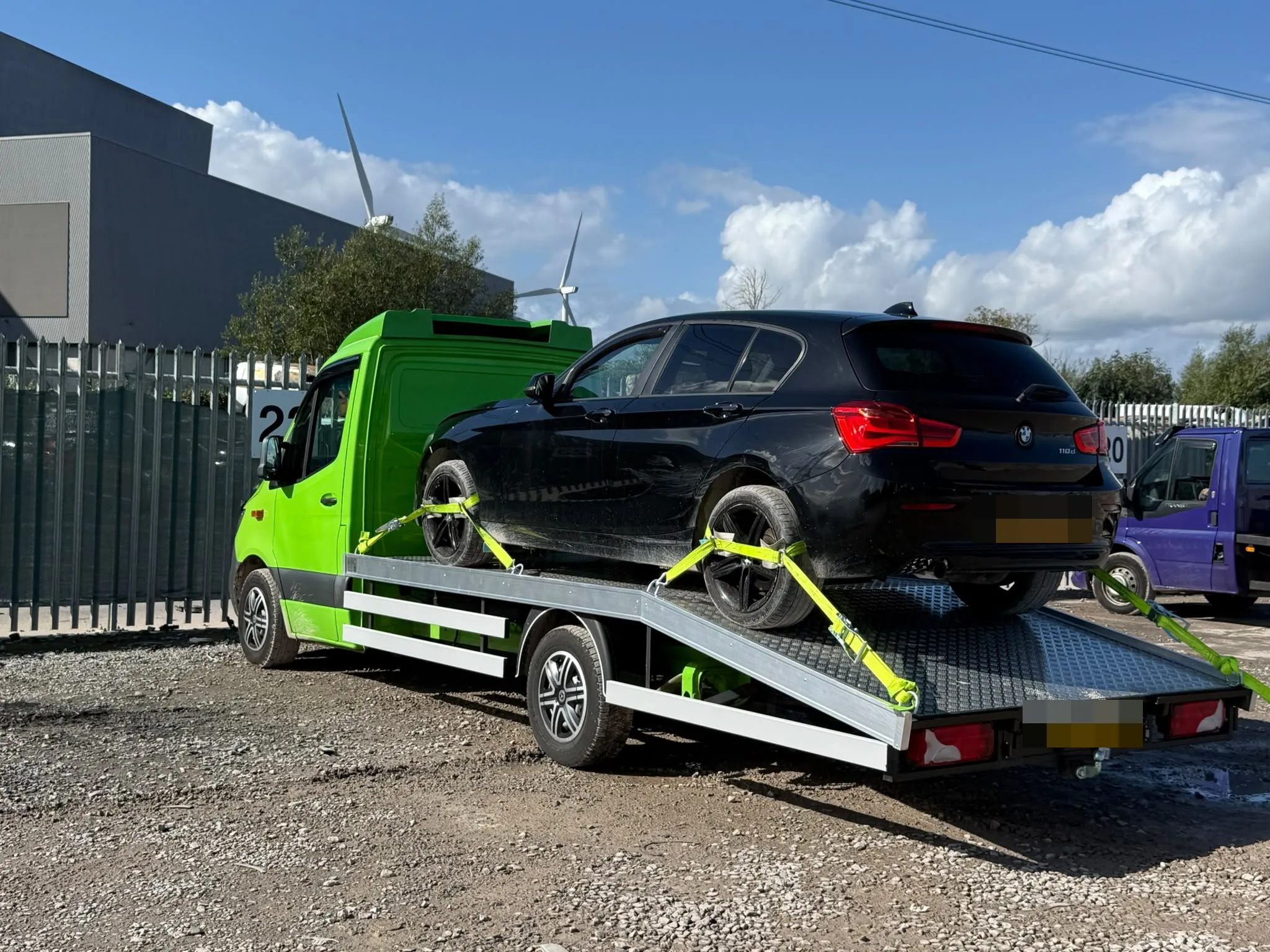 Black BMW strapped at all four wheels on the tilted flatbed in a yard