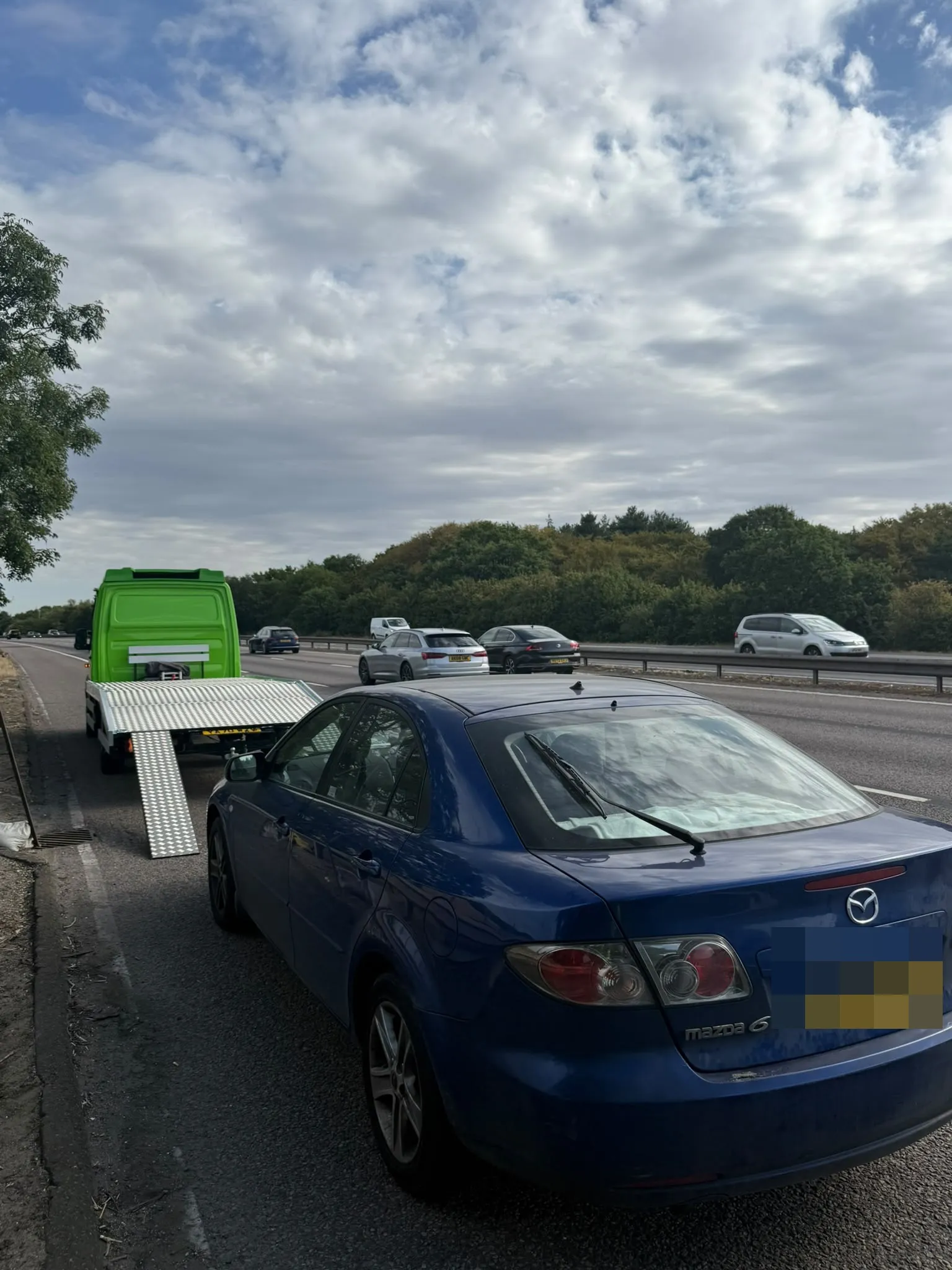 Blue Mazda waiting behind the flatbed on a dual carriageway hard strip