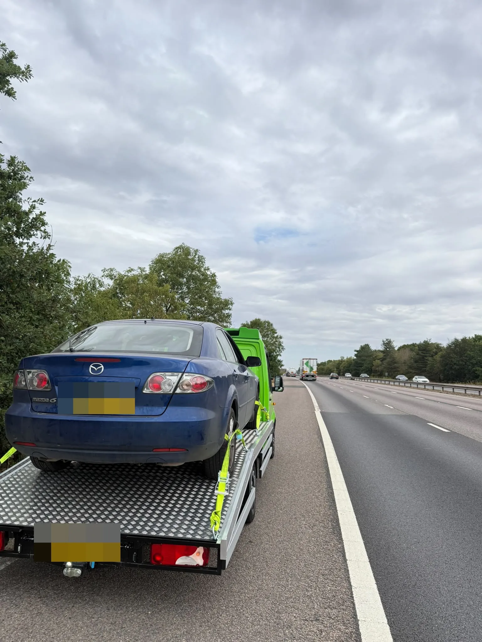 Blue Mazda strapped on the flatbed at the side of a dual carriageway