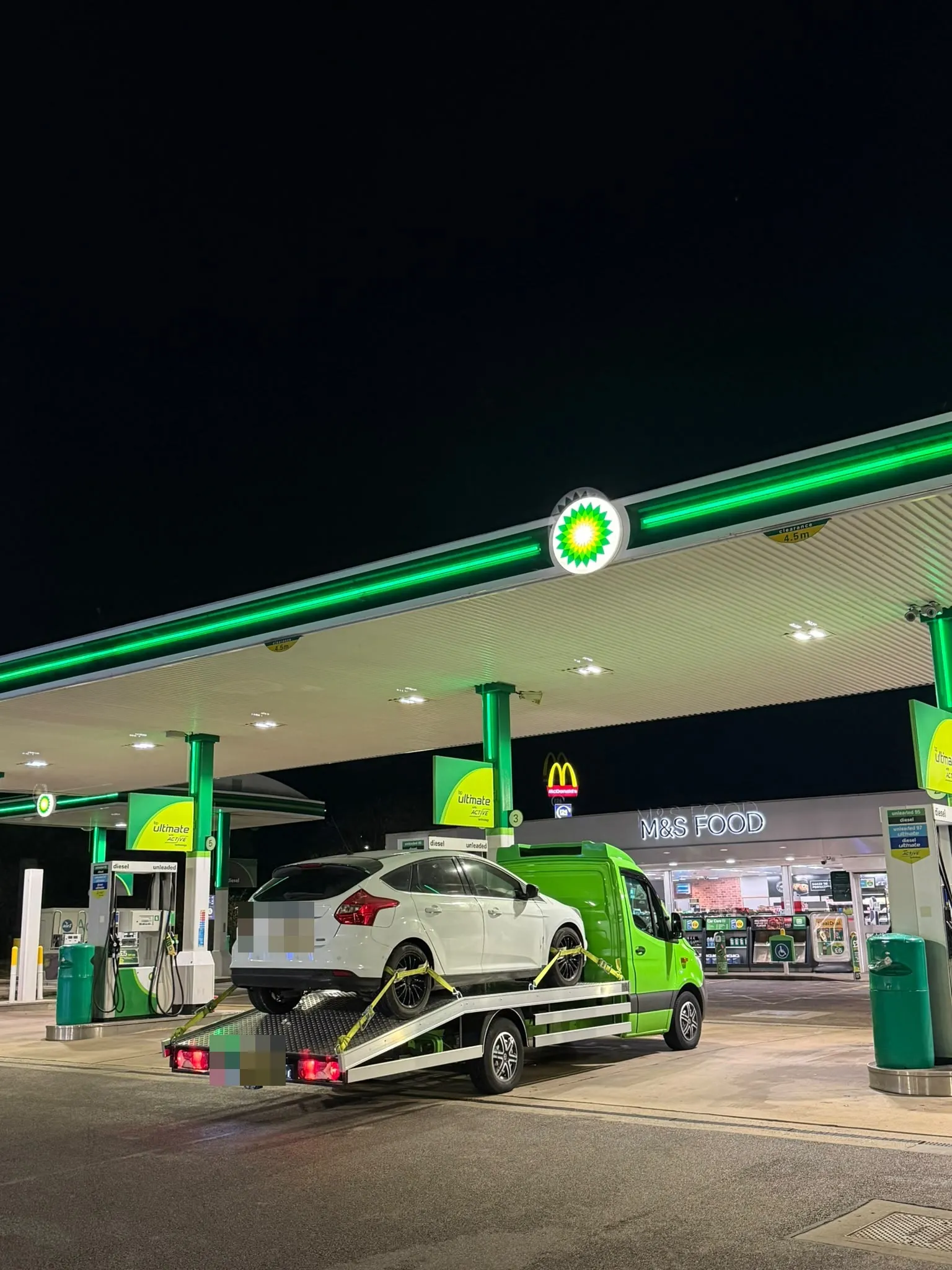 White Ford Focus on the flatbed at a petrol station at night