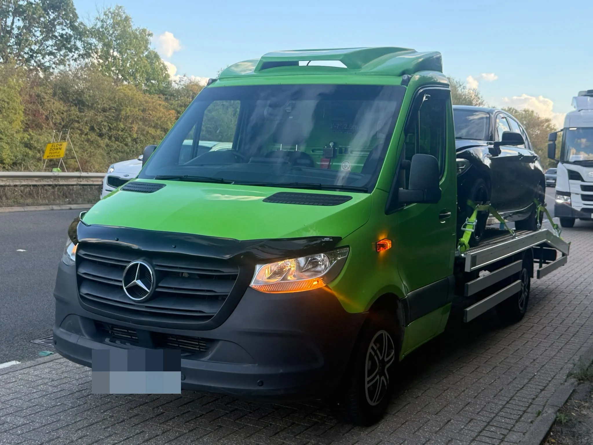 Toma Recovery's lime green Mercedes-Benz Sprinter flatbed at dusk with its lights on