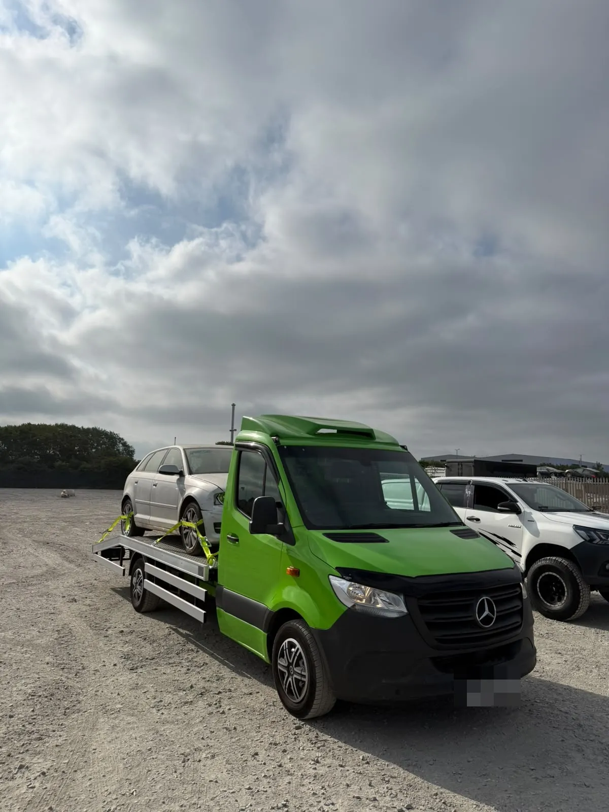 Toma Recovery's lime green Mercedes-Benz Sprinter flatbed in a yard with a silver car on board